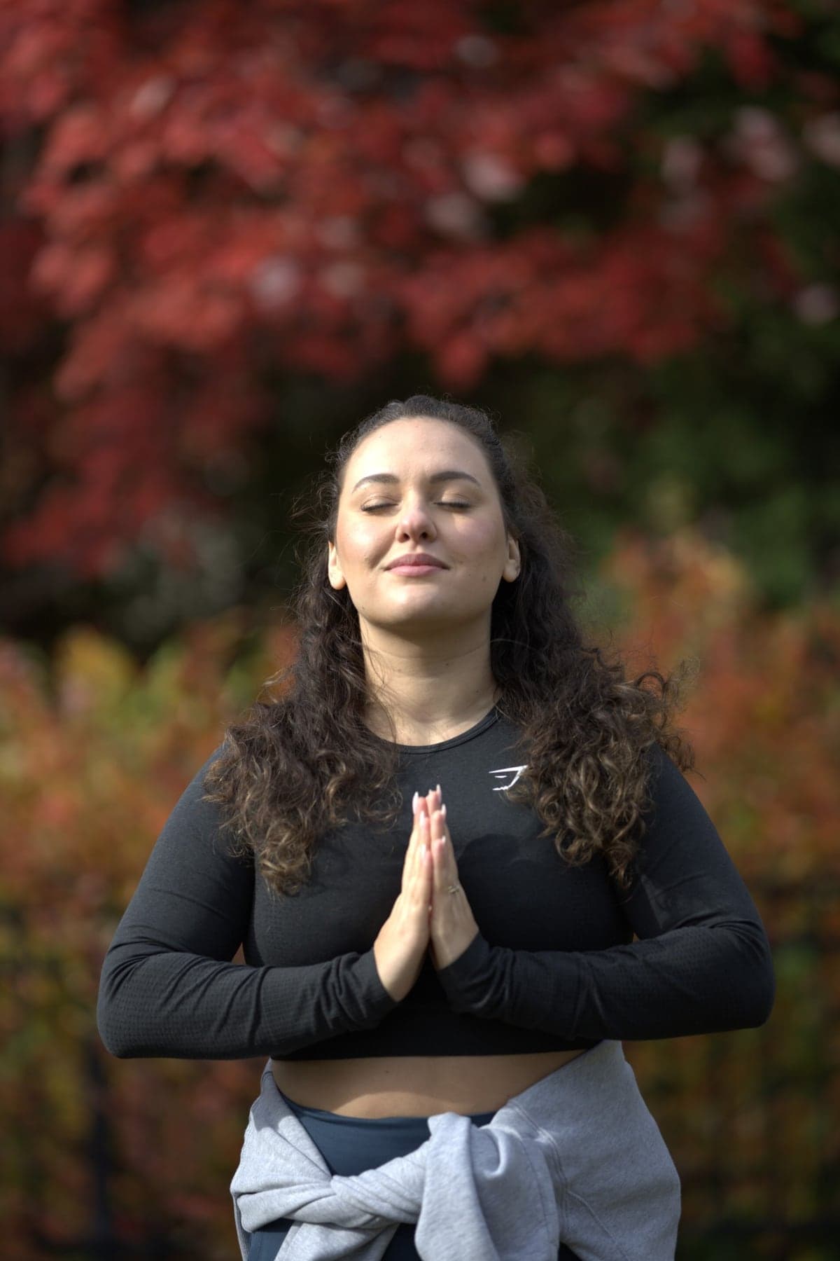Coach Georgie, eyes closed and hands together, in front of autumn foliage